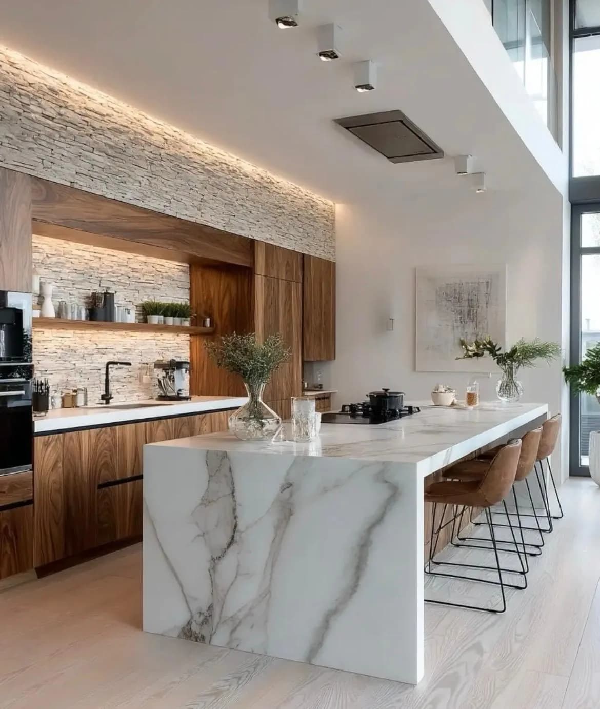 Cocina moderna abierta al salón con isla central de gran tamaño, encimera clara y taburetes altos.